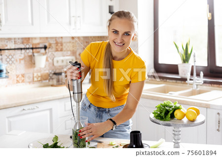 A young woman with a blender and green vegetables making a detox cocktail. Healthy food, cooking, vegetarian food, diet A young woman with a blender and green vegetables making a detox cocktail. Healthy food, cooking, vegetarian food, diet 75601894