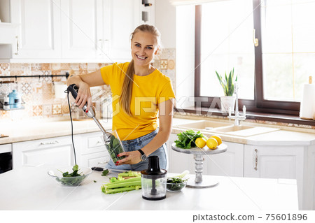 A young woman with a blender and green vegetables making a detox cocktail. Healthy food, cooking, vegetarian food, diet 75601896