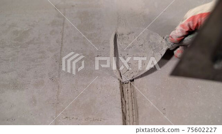 Close-up of a hand with a trowel and plaster while repairing a wall. The worker is filling the cracks with plaster. Close-up of a hand with a trowel and plaster while repairing a wall. The worker is filling the cracks with plaster. 75602227