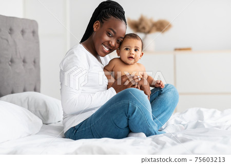 African American mom sitting on bed with her cute baby African American mom sitting on bed with her cute baby 75603213