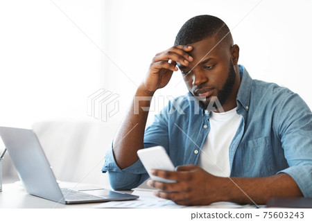 Concerned black freelancer guy looking at smartphone while working at home office 75603243