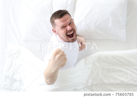 Young man lying in bed and rejoicing top view 75603785