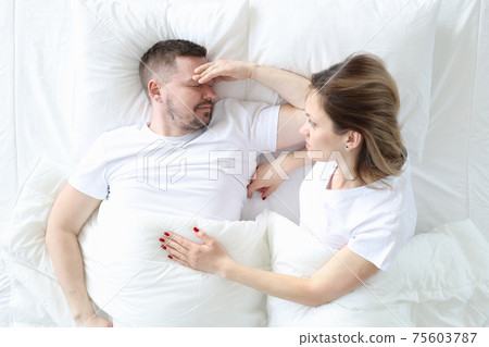Married couple is lying in bed top view. Man holding his head Married couple is lying in bed top view. Man holding his head 75603787