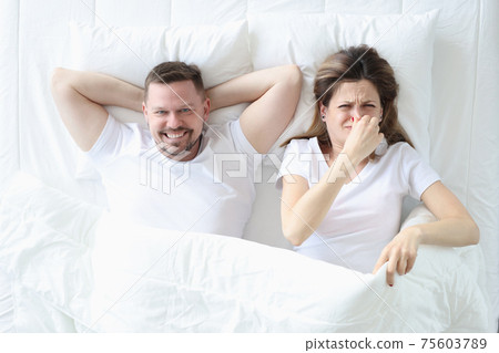 Woman lying in bed with man and covering her nose with her hand 75603789