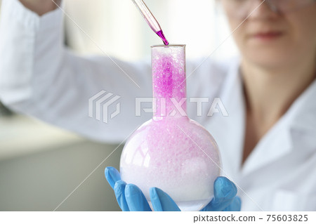 Woman scientist dripping liquid from pipette into chemical flask closeup 75603825