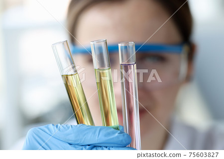 Woman scientist holding test tubes with multicolored liquids in her hands closeup 75603827