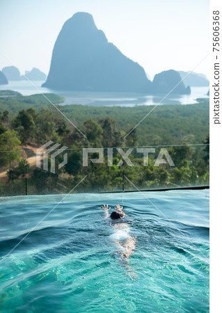 Happy woman in white swimsuit swimming in luxury pool hotel against Phang Nga bay background, Tourist relaxing at Samet Nang She, near Phuket in Southern Thailand. travel, trip and summer vacation 75606368