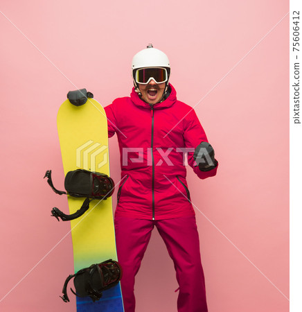 Male snowboarder with skiing gear in bright ski suit isolated on pink background Male snowboarder with skiing gear in bright ski suit isolated on pink background 75606412