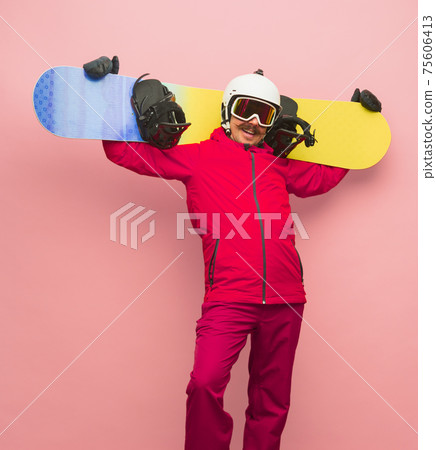 Male snowboarder with skiing gear in bright ski suit isolated on pink background Male snowboarder with skiing gear in bright ski suit isolated on pink background 75606413