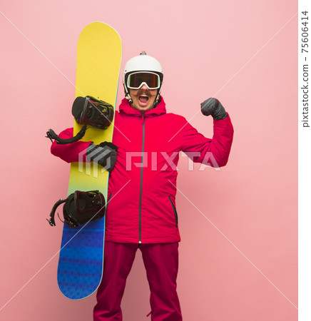 Male snowboarder with skiing gear in bright ski suit isolated on pink background Male snowboarder with skiing gear in bright ski suit isolated on pink background 75606414