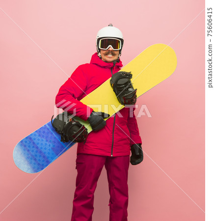 Male snowboarder with skiing gear in bright ski suit isolated on pink background Male snowboarder with skiing gear in bright ski suit isolated on pink background 75606415