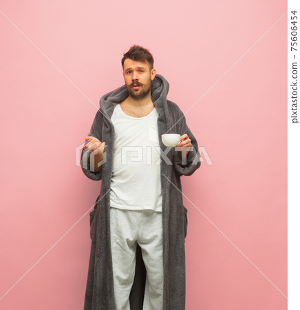 Sleepy man in gray bathrobe and cup of coffee isolated on pink background Sleepy man in gray bathrobe and cup of coffee isolated on pink background 75606454