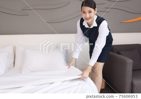 Asia maid making bed in hotel room, setting up pillow on bed 75606953