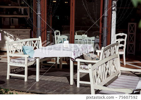 outdoor cafe terrace with tables with a tablecloth with benches for sitting with cushions on a wooden deck on a sunny summer day, nobody. 75607592
