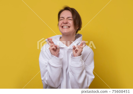 Caucasian woman closing her eyes, crossing her fingers hoping for the best. 75608451