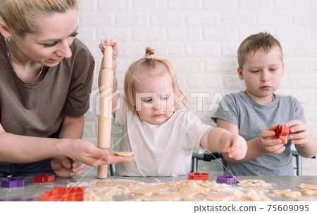 little girl and boy help mom in the kitchen to cook delicious cookies 75609095
