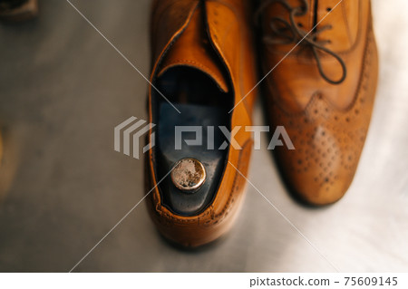 Close-up view of old light brown leather shoes with wooden shoe pad to be repaired in dark craft shoe shop. 75609145