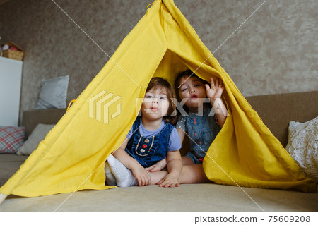 two little girls play at home in yellow in a teepee two little girls play at home in yellow in a teepee 75609208