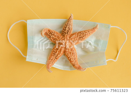 Star fish and face medical mask on yellow background. Coronavirus travel concept. Minimal 75611323