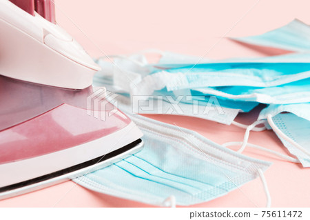 Iron and face medical masks on the ironing board. Reuse of face masks concept 75611472