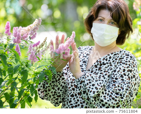 Allegria woman with mask on face near flowering bush 75611804