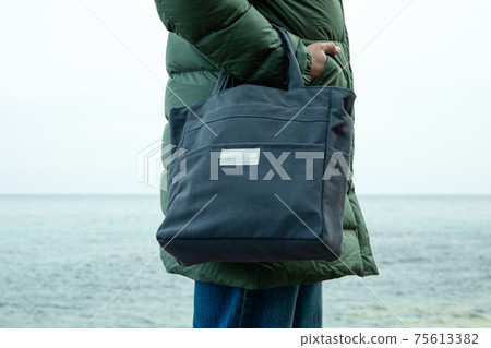 Woman in winter clothing with stylish eco bag on sea shore Woman in winter clothing with stylish eco bag on sea shore 75613382