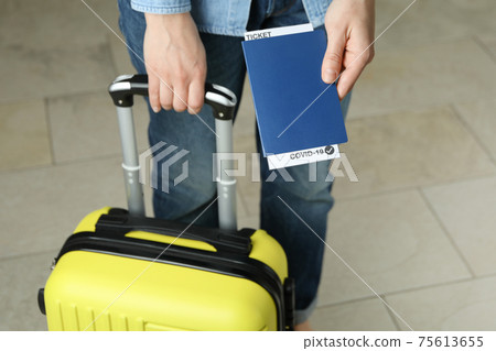 Woman hold suitcase and passport with ticket and COVID - 19 mark Woman hold suitcase and passport with ticket and COVID - 19 mark 75613655