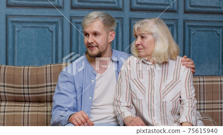 Happy grown adult son laughing embracing talking to best friend older senior mother sit on sofa Happy grown adult son laughing embracing talking to best friend older senior mother sit on sofa 75615940