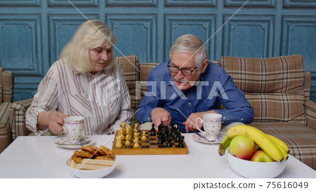 Retired senior couple talking drinking tea, playing chess in modern living home room lounge together 75616049