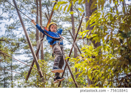 Happy child in a helmet, healthy teenager school boy enjoying activity in a climbing adventure park on a summer day 75618841