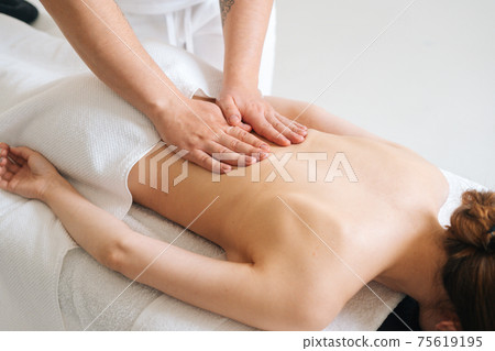 Top view of male masseur massaging back of young unrecognizable woman lying on massage table. 75619195