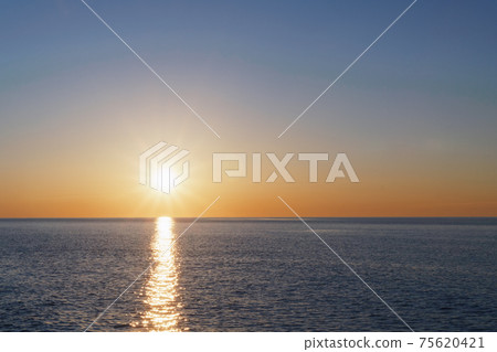 The setting sun goes into the sea on the horizon with a light track and reflections on the sea. The setting sun goes into the sea on the horizon with a light track and reflections on the sea. 75620421