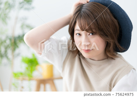 Portrait of a young woman trying to wear a blue straw hat in the living room Portrait of a young woman trying to wear a blue straw hat in the living room 75624975
