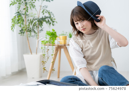 Portrait of a young woman trying to wear a blue straw hat in the living room Portrait of a young woman trying to wear a blue straw hat in the living room 75624978