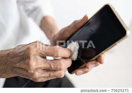 Hands of old elderly using cotton wool with alcohol to wipe the phone screen,cleaning smart phone,stop spreading Coronavirus,COVID-19 outbreak,concept of wipe clean surface that are frequently touched 75625271