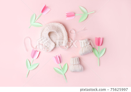 Bonnet and booties on a pink background. Handmade clothes for a newborn, decorative paper flowers. Newborn baby gift concept, mom's day, first birthday, first wardrobe, outfit Bonnet and booties on a pink background. Handmade clothes for a newborn, decorative paper flowers. Newborn baby gift concept, mom's day, first birthday, first wardrobe, outfit 75625997