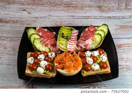Assorted sandwiches with fish, cheese, meat and vegetables on a black plate and wooden background Assorted sandwiches with fish, cheese, meat and vegetables on a black plate and wooden background 75627002