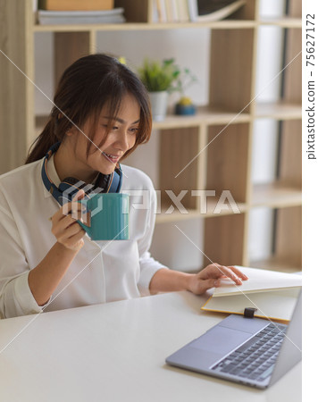 Female student relaxing with coffee while doing assignment in living room at home Female student relaxing with coffee while doing assignment in living room at home 75627172