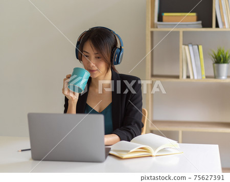 Portrait of businesswoman working from home, using laptop, head phone and drinking coffee 75627391