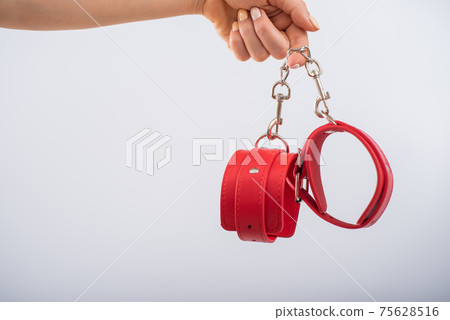 Red leather handcuffs in female hands on a white background. BDSM accessories 75628516