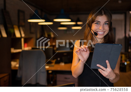 Beautiful business woman wearing in a headset is holding a digital tablet in the office 75628558