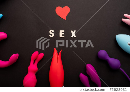 The inscription sex heart and a collection of multicolored vibrators on a black background. Sex toys of various shapes. Assortment of sex shop The inscription sex heart and a collection of multicolored vibrators on a black background. Sex toys of various shapes. Assortment of sex shop 75628981