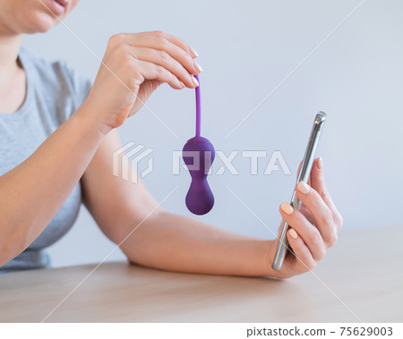 The girl synchronizes the kegel trainer with the application on the smartphone. A woman is holding a sex toy to strengthen the pelvic floor muscles 75629003