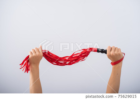 Red leather whip in female hands on a white background. Copy space. 75629015
