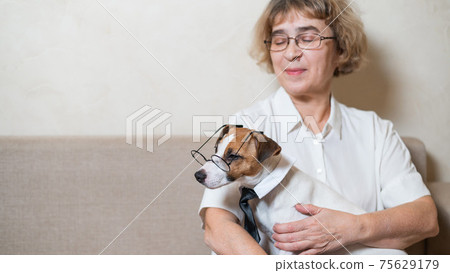 An elderly caucasian woman is holding a smart dog Jack Russell Terrier wearing glasses and a tie An elderly caucasian woman is holding a smart dog Jack Russell Terrier wearing glasses and a tie 75629179