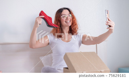 Caucasian woman sitting in bed and taking a selfie with a delivered purchase. Online shopping for shoes Caucasian woman sitting in bed and taking a selfie with a delivered purchase. Online shopping for shoes 75629181