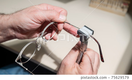 The man bends the temples of his glasses. The master repairs the frame with tongs. 75629579