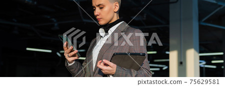 Pensive young woman with short hair uses mobile phone in office. Pensive young woman with short hair uses mobile phone in office. 75629581