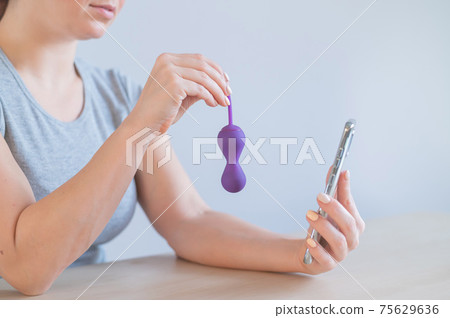 A female blogger recommends a kegel trainer online over the phone. A woman is holding a sex toy to strengthen the pelvic floor muscles 75629636