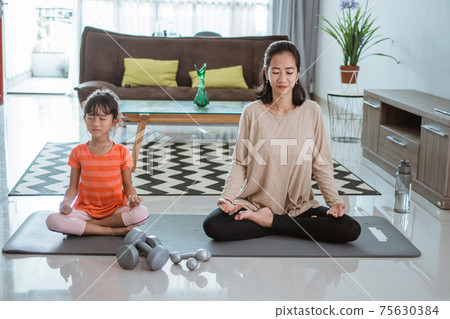 mother doing yoga exercise at at home with her daughter together mother doing yoga exercise at at home with her daughter together 75630384